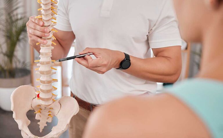 A person seated at a desk adjusting their sitting position to maintain upright posture.